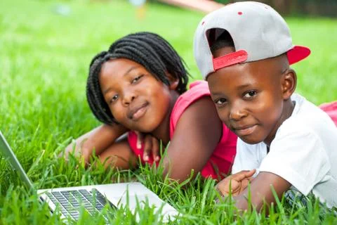 African kids laying on grass with laptop. Foto stock