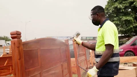 African male carpenter using a spray gun to varnish wooden bed frame Stock Footage 346734002