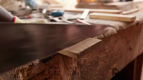 African male carpenter in work gloves saws a wooden plank with a hand saw Stock Footage 346733698