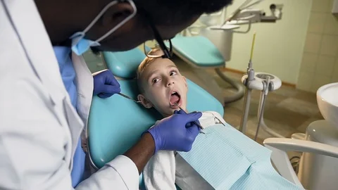 African male dentist checking the teeth of little male patient. Stock Footage 104146353