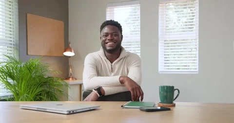 African male wearing pullover sitting at desk, blinking smiling and laughing at Stock Footage 343888914