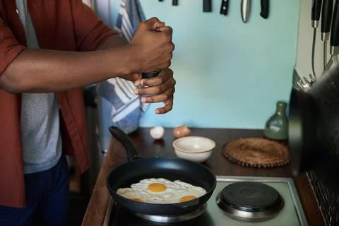 African man adding salt to some eggs in a frypan Stock Photos