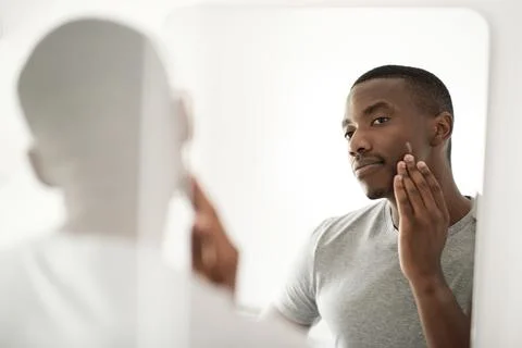African man applying lotion on his face in his bathroom mirror Stock Photos