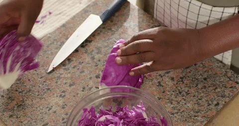 African man in apron placing halved purple cabbage on counter, shredding with Stock Footage 341944737