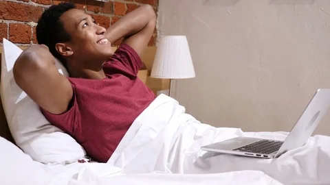 African Man in Bed Working on Laptop and Reacting to Success Stock Footage 83873023