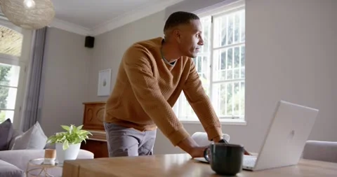 African man bending leaning over table using laptop touching mug brown knit Stock Footage 339252815