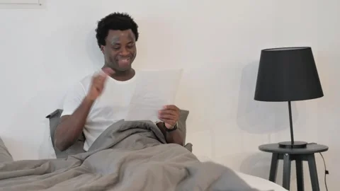 African Man Celebrating while Reading Documents in Bed Stockbeeldmateriaal 299756227