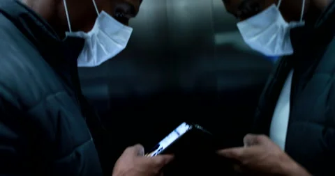 African man checking cellphone wearing covid-19 mask inside elevator looking  Stockbeeldmateriaal 130546119