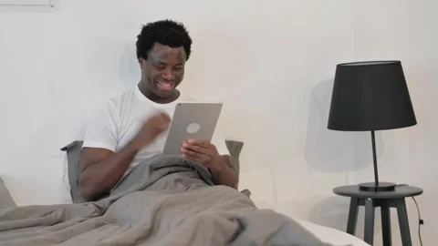 African Man Cheering Win on Tablet while Sitting on Sofa at Home Stock Footage 299756018