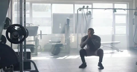 African man in compression top doing squat reps starting low by rack in gym, Stock Footage 337885880