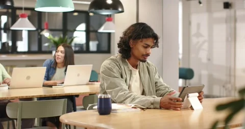 African man at coworking table tapping tablet on stand while working, woman Stock Footage 340969160