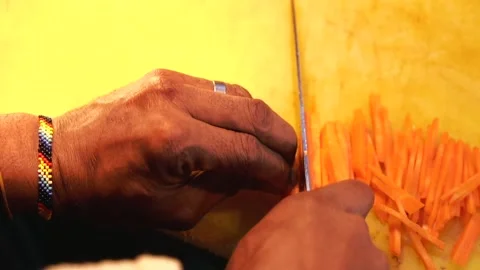 African man cutting vegetables with a sharp knife using a yellow cutting board Stock Footage 230080409