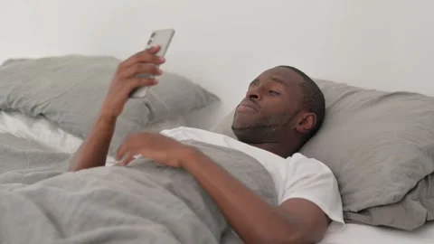 African Man Doing Video Chat on Phone while Lying in Bed 스톡 동영상 287902922