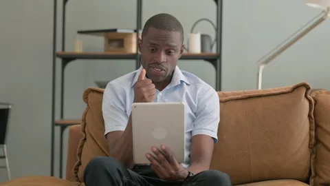African Man Doing Video Chat on Tablet while Sitting on Sofa at Home Stock Footage 287914895
