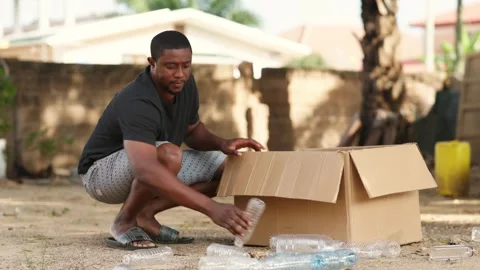 African Man Fills Box with Plastic Bottles for Recycling Outdoors Video stock 346243761