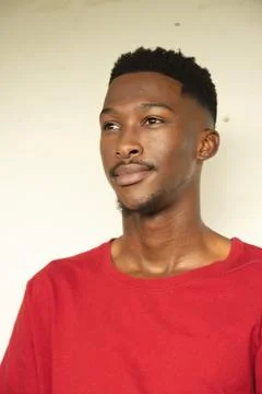 African man gazing off-camera, posing in studio with red crewneck T-shirt plain Stock Photos
