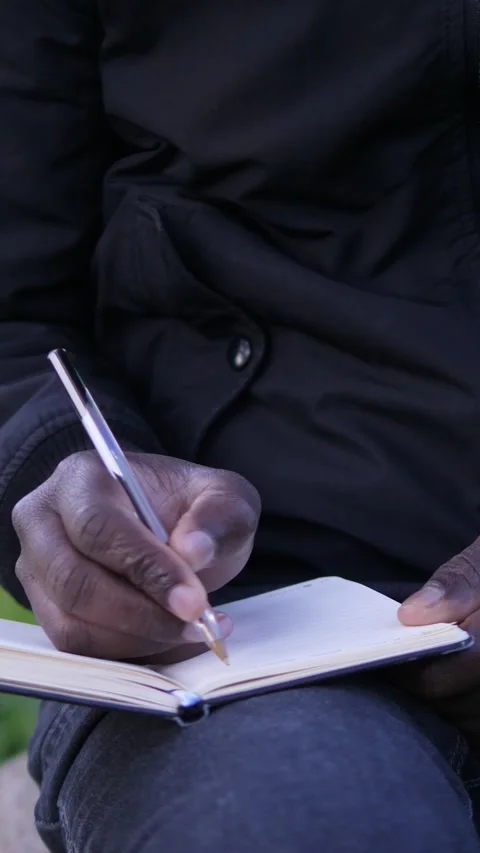 African man hands writing personal thoughts in small notebook outdoors Stock Footage 335696510
