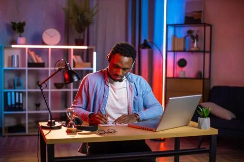 African man in headset taking notes during video call 库存照片