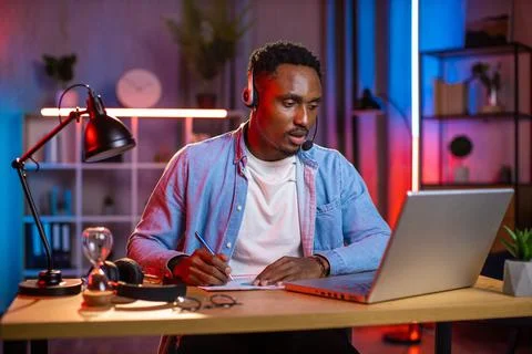 African man in headset taking notes during video call 库存照片