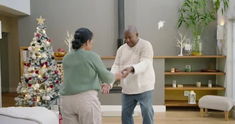 African man leading turns joining hands with senior woman by Xmas tree and Stock Footage 342995970