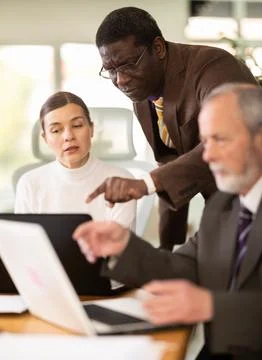 African man leaned over to seated female employee, helps with work and looks at Stock Photos