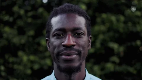 African man looking at camera with green park on background Stock Footage 239561232