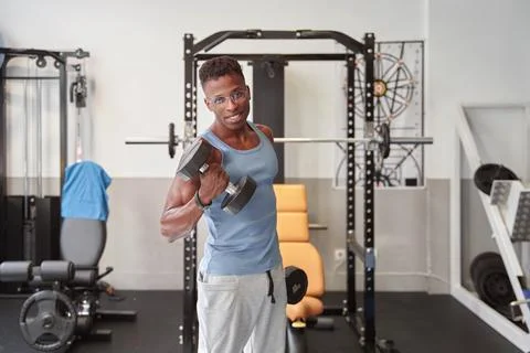 African man looking at the camera while doing weights at the gym Foto stock