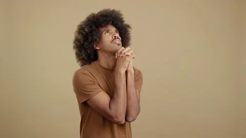 African man looking up while praying with folded hands Stock Footage 231038525