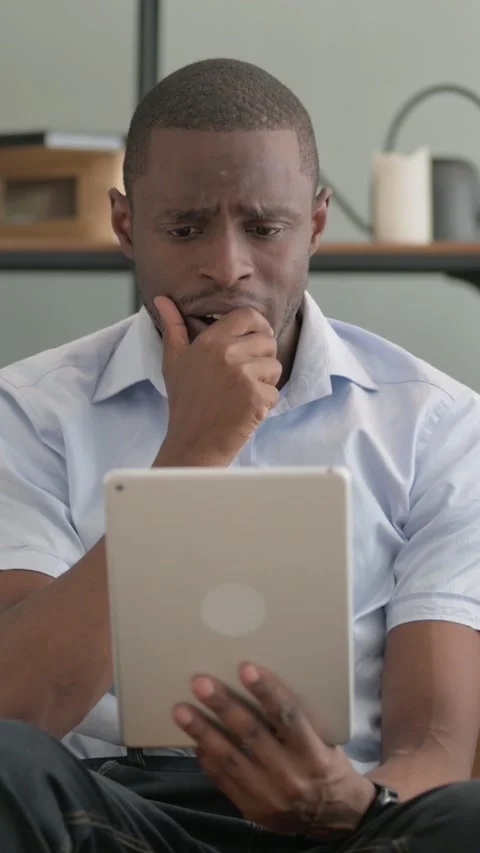 African Man with Loss on Tablet while Sitting on Sofa at Home Stock Footage 301856453