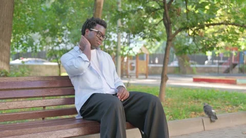 African Man Massaging Neck while Sitting in the Park Vídeo Stock 316805057