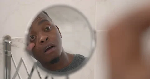 African man in mirror reflection examining his eyes. Rubbing tired eyes. Stock Footage 153287625