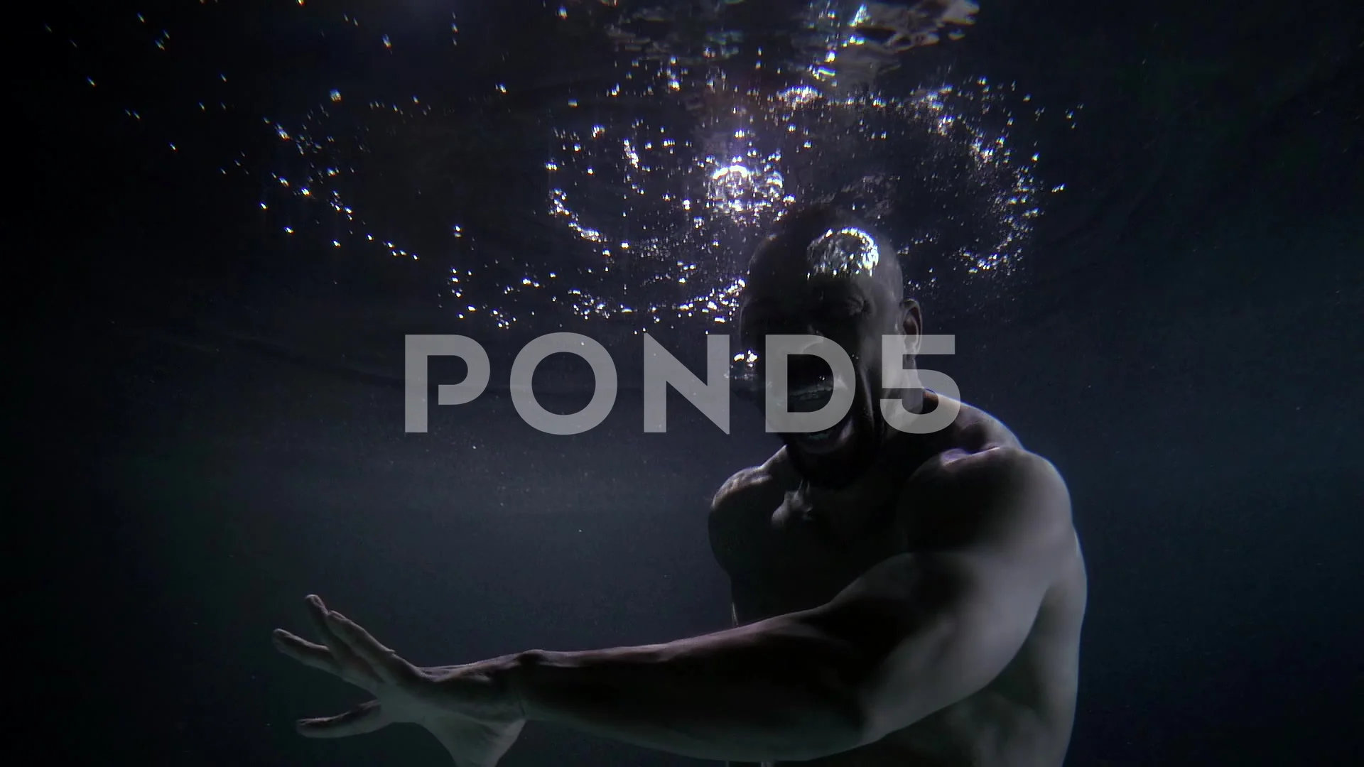 an African man with a naked torso floats in the dark water. he moves his  hands