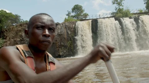 African man paddles raft on river with waterfalls Vídeo Stock 128284553