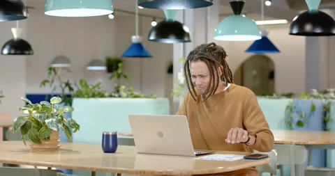 African man pausing, inspecting laptop, comparing paper charts at coworking Stock Footage 335747467