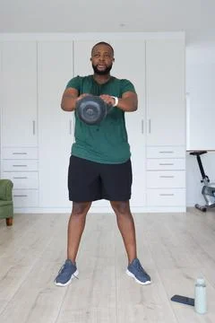 African man performing kettlebell exercise in bright home workout room with Stock Photos