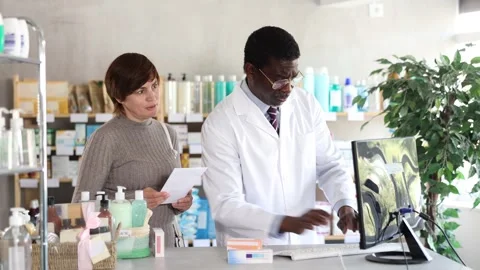 African man pharmacist uses computer at workplace and consulting woman client Stock Footage 347257478