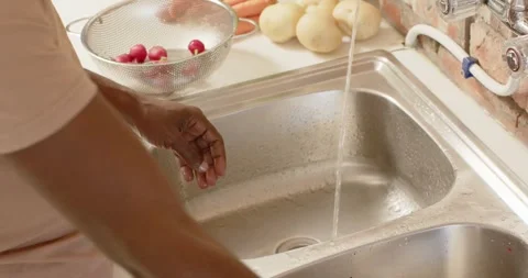 African man picking radishes from colander at kitchen sink, rinsing and rubbing Stock Footage 342023331