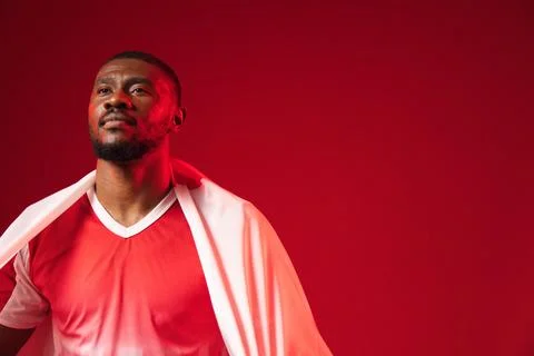 African man posing in studio under lighting, wearing red V-neck shirt, white Stock Photos