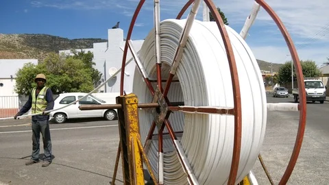 African man pulling optical fibre internet cable from a large revolving roll Stock Footage 103290710