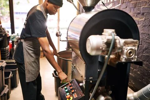 African man pushing red button on an industrial coffee machine Stock Photos