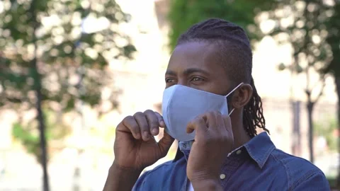 African man puts on protective face mask looking away standing on the street Stock-Footage 157525462