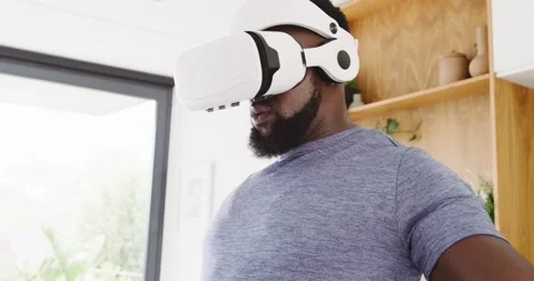 African man putting on white VR headset, reaching and selecting virtual objects 스톡 동영상 344318705