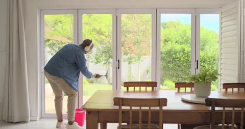 African man reaching red bucket, dipping squeegee, cleaning sliding door in Stock Footage 341320741