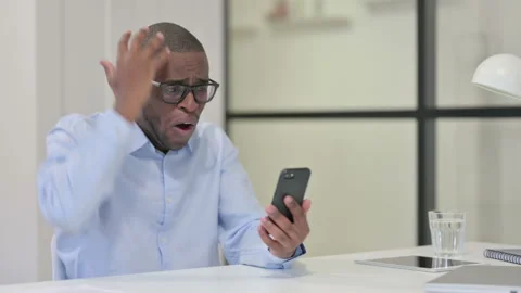 African Man Reacting Loss while using Smartphone Stock Footage 144735433