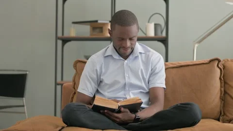 African Man Reading Book while Sitting on Sofa at Home Video stock 287918433