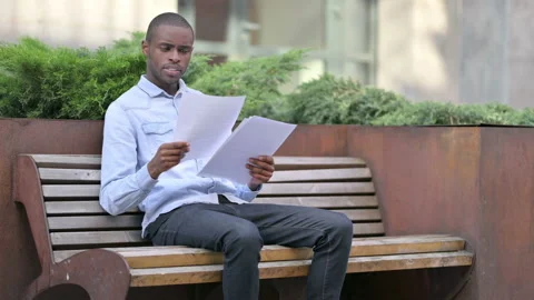 African Man Reading Documents sitting Outdoor Stock Footage 136032785
