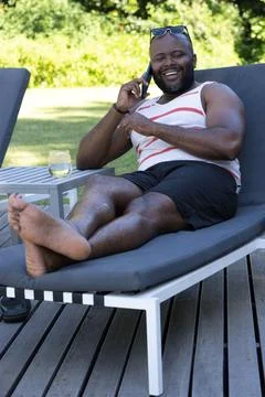 African man reclining on backyard deck lounger, wearing sunglasses, holding Stock Photos