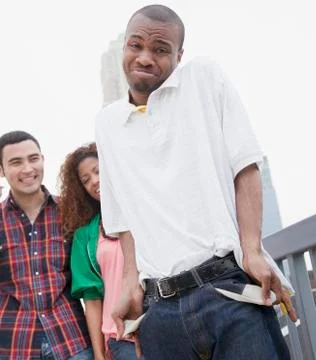 African man showing empty pockets with friends in background Stock Photos