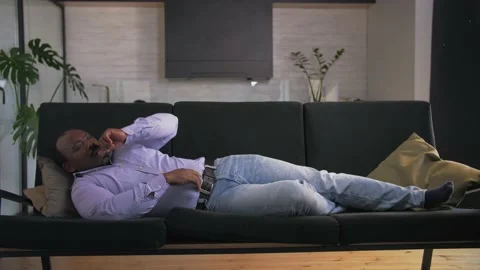 African man is sick. Lying on the couch and coughing.Wide Shot Stock Footage 201292120