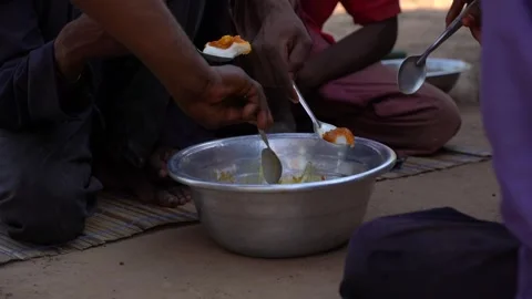 African man sitting on the ground sharing meal out of one pot Stock Footage 243590818